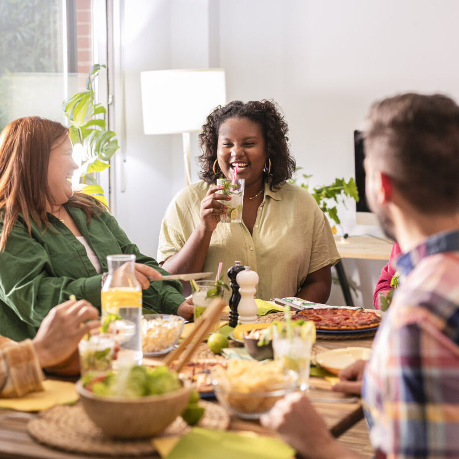 Diverse group of friends enjoying a dinner party at home, laughing and eating pizza and cocktails, creating lasting memories and bonding over a healthy meal