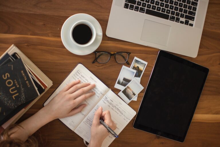 Overhead view of person at laptop, drinking coffee and writing in journal